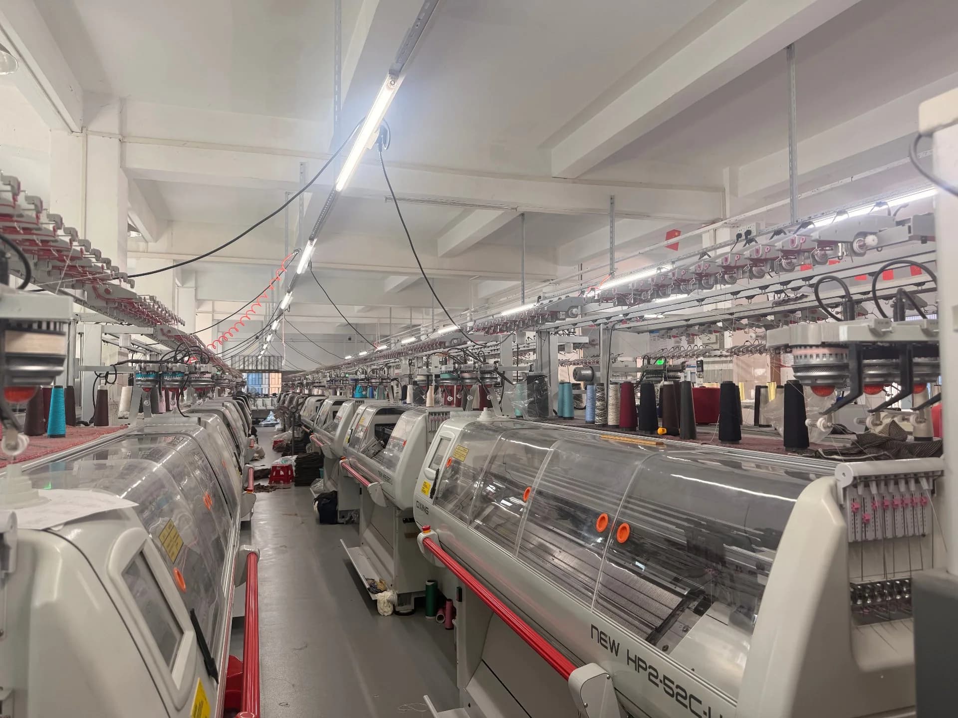 Knitted panels folded in trays beneath flat-bed knitting machines, awaiting collection